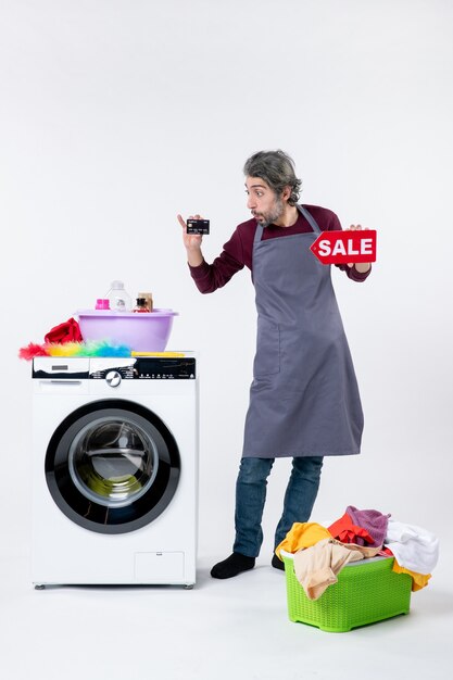 Photo gratuite vue de face un homme confus tenant une carte et un signe de vente debout près du panier à linge de la laveuse sur fond blanc isolé