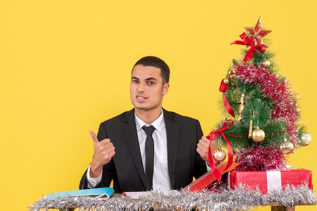 Vue de face homme en costume assis à la table tenant un document montrant quelque chose d'arbre de Noël et de cadeaux