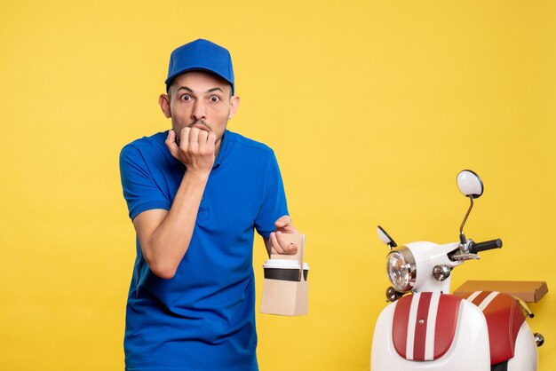 Vue de face homme courrier tenant le café de livraison sur le vélo de service de travail uniforme de travailleur de couleur jaune