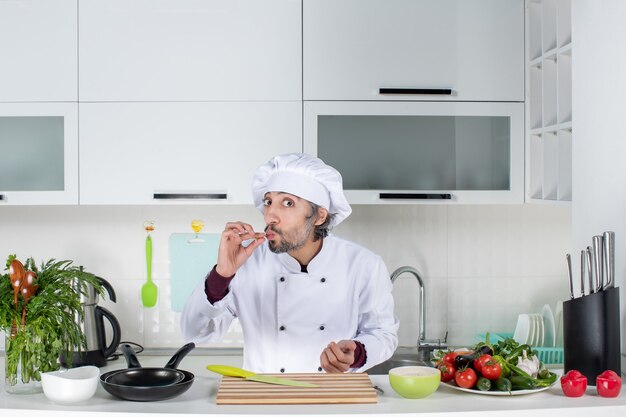 Vue de face homme cuisinier en uniforme faisant un baiser de chef dans la cuisine