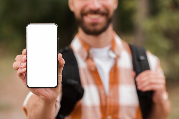 Vue de face de l'homme défocalisé avec sac à dos tenant le smartphone