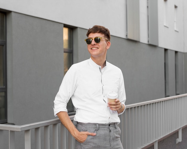 Vue de face de l'homme élégant avec des lunettes de soleil tenant une tasse de café à l'extérieur