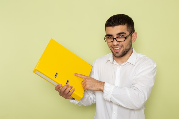 Photo gratuite vue de face de l'homme employé de bureau en chemise blanche tenant un fichier jaune sur le mur vert clair