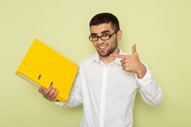 Vue de face de l'homme employé de bureau en chemise blanche tenant des fichiers jaunes avec sourire sur le mur vert