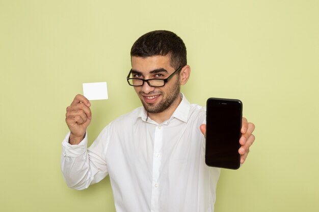 Vue de face de l'homme employé de bureau en chemise blanche tenant le smartphone et la carte sur un mur vert clair