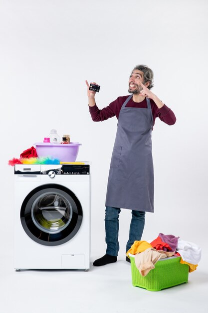 Vue de face homme exalté tenant une carte debout près du panier à linge de la machine à laver sur fond blanc