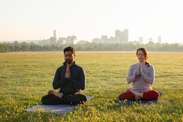 Vue de face de l'homme et de la femme méditant à l'extérieur sur des tapis de yoga