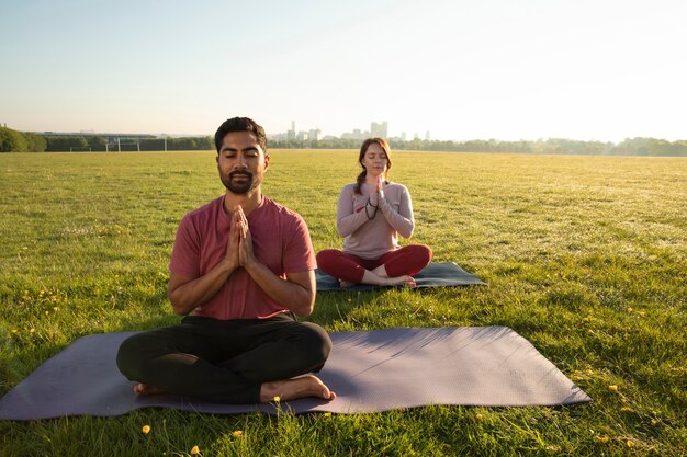 Vue de face de l'homme et de la femme méditant à l'extérieur sur des tapis de yoga