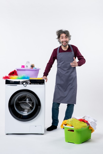 Vue de face homme de femme de ménage heureux debout près du panier à linge de la laveuse sur fond blanc