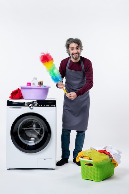 Vue de face homme de femme de ménage heureux tenant un plumeau debout près de la machine à laver sur fond blanc