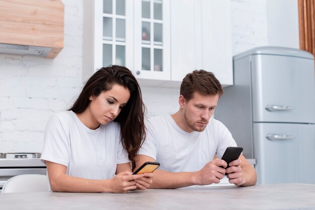 Vue de face homme et femme vérifiant leurs téléphones dans la cuisine