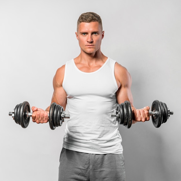 Vue de face de l'homme en forme avec débardeur à l'aide de poids