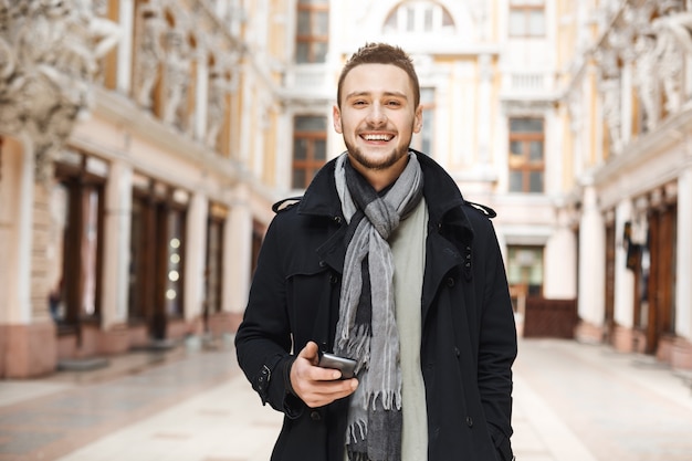 Vue de face de l'homme gai tenant le téléphone et regardant droit.