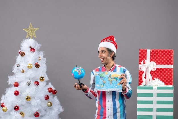 Vue de face homme heureux avec bonnet de noel printemps en spirale tenant la carte du monde et le globe