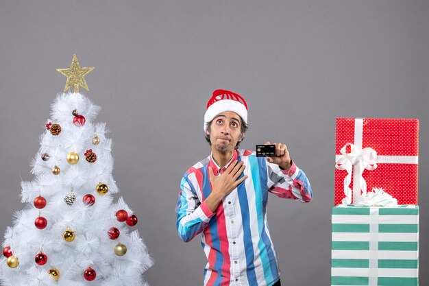 Vue de face homme heureux mettant la main dans sa poitrine debout près de l'arbre de Noël blanc