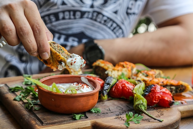 Vue de face homme mangeant le lula kebab dans du pain pita avec des tomates au yogourt et des piments grillés sur un plateau