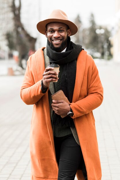 Vue de face homme en manteau orange tenant une tasse de café en plein air