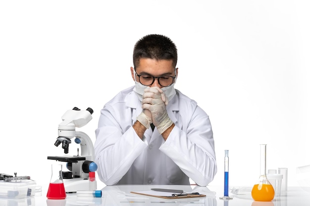 Vue de face de l'homme médecin en costume médical blanc et avec masque en pensant profondément sur l'espace blanc