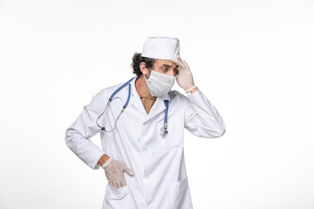 Vue de face de l'homme médecin en costume médical avec masque comme protection contre les covid- réflexion sur la pandémie de coronavirus virus splash mur blanc