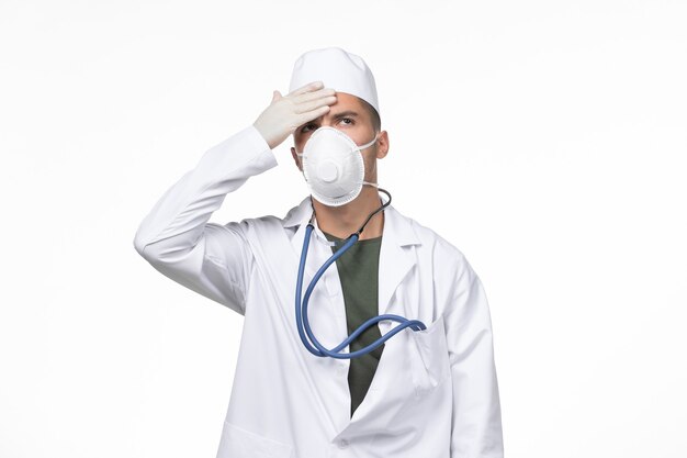 Vue de face de l'homme médecin en costume médical et masque contre le coronavirus sur mur blanc covid- pandémie d'isolement de maladie de maladie de virus