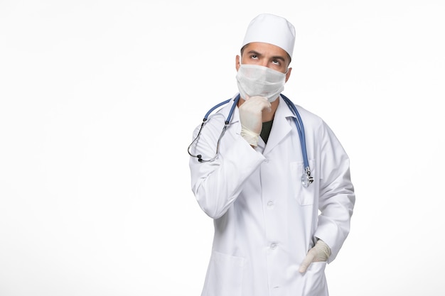 Vue de face de l'homme médecin en costume médical et masque contre la pensée de coronavirus sur mur blanc pandémie d'isolement de maladie de maladie de covid- virus