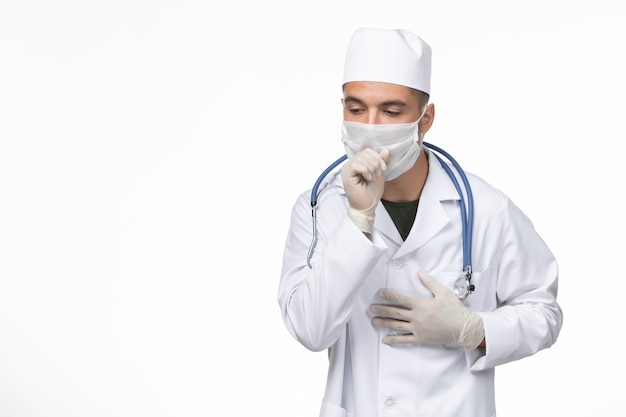 Vue de face de l'homme médecin en costume médical et masque contre la toux de coronavirus sur mur blanc covid- pandémie d'isolement de maladie de maladie de virus