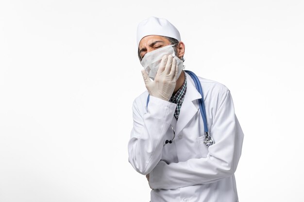 Vue de face de l'homme médecin en costume médical et masque en raison d'un coronavirus sur une surface blanche