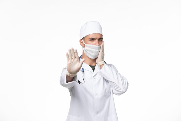 Vue de face de l'homme médecin en costume médical et portant un masque contre covid sur la pandémie de médecine virus covid mur blanc clair