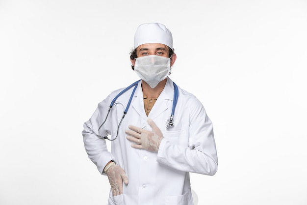 Vue de face de l'homme médecin en costume médical portant un masque stérile comme une protection contre le covid sur la maladie pandémique du coronavirus virus mur blanc