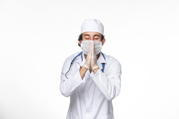 Vue de face de l'homme médecin en costume médical portant un masque stérile comme protection contre le covid sur la pandémie de coronavirus de virus de splash de bureau blanc