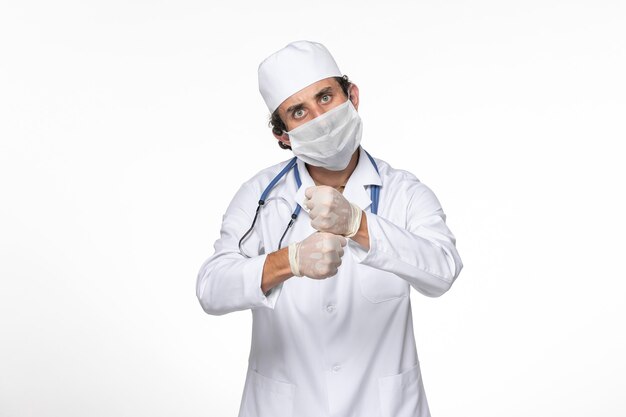 Vue de face de l'homme médecin en costume médical portant un masque stérile comme une protection contre le covid sur la pandémie de coronavirus virus splash mur blanc