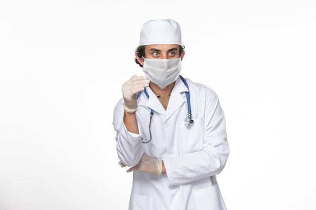 Vue de face de l'homme médecin en costume médical portant un masque stérile comme une protection contre le covid sur la pandémie de coronavirus virus splash mur blanc