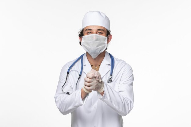 Vue de face de l'homme médecin en costume médical portant un masque stérile comme protection contre le covid se serrant la main sur la maladie pandémique du coronavirus virus mur blanc