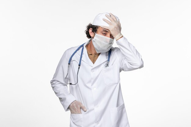 Vue de face de l'homme médecin en costume médical portant un masque stérile comme une protection contre le covid a souligné sur la maladie de la maladie pandémique du coronavirus virus mur blanc