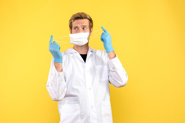 Vue de face de l'homme médecin décollant le masque sur la santé de covid pandémique fond jaune