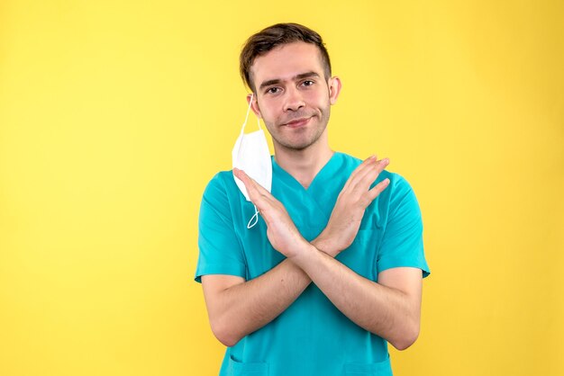 Vue de face de l'homme médecin décoller son masque sur mur jaune