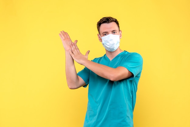 Vue de face de l'homme médecin avec masque applaudissant sur mur jaune