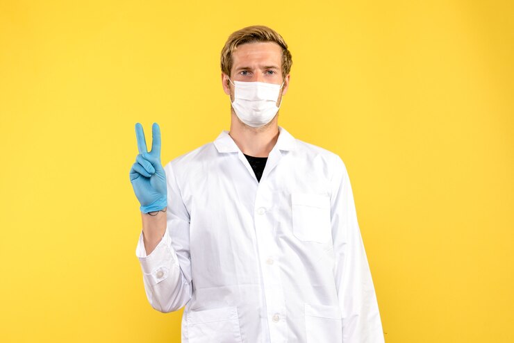 Photo gratuit vue de face de l'homme médecin en masque sur fond jaune pandémie médicale covid medic