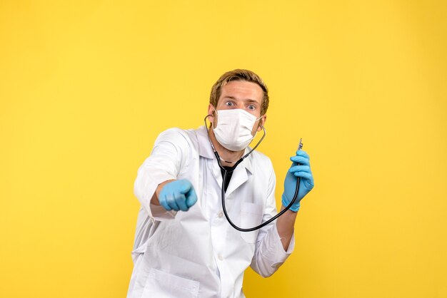 Vue de face de l'homme médecin en masque avec stéthoscope sur fond jaune pandémie de santé covid