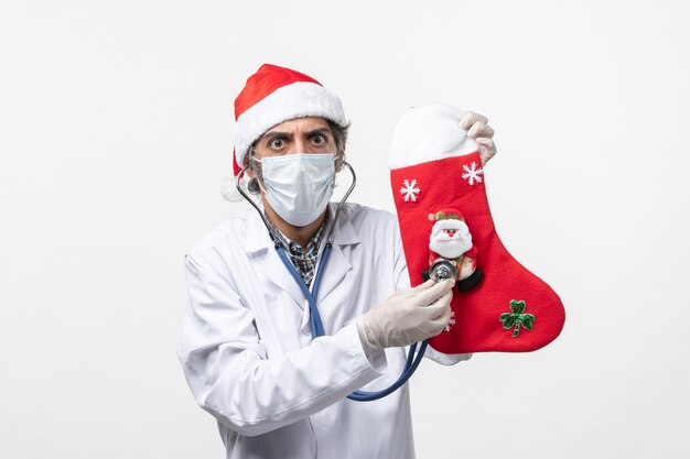 Vue de face de l'homme médecin observant la chaussette de vacances sur le mur blanc vacances virus covid