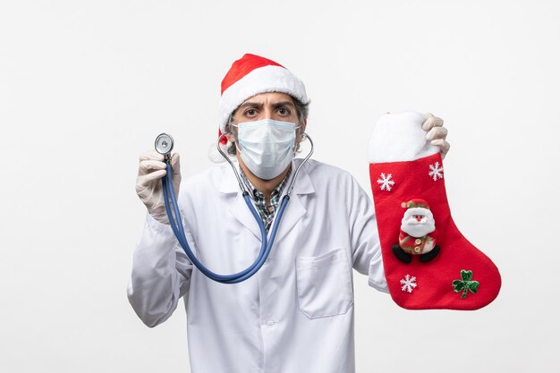 Vue de face de l'homme médecin observant la chaussette de vacances sur le sol blanc vacances virus covid