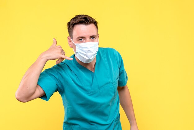 Vue de face de l'homme médecin portant un masque sur mur jaune