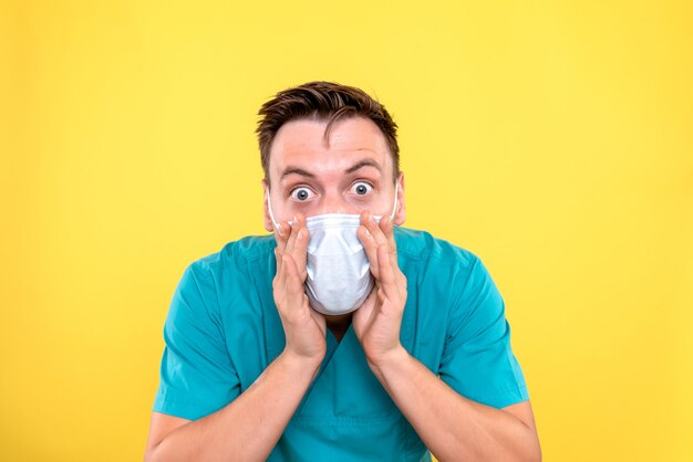 Vue de face de l'homme médecin portant un masque stérile sur mur jaune