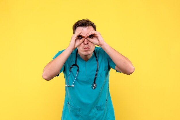 Vue de face de l'homme médecin regardant à travers ses doigts sur le mur jaune