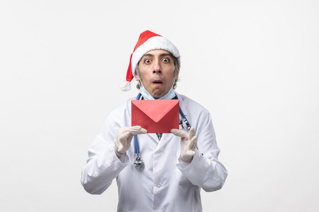 Vue de face de l'homme médecin tenant une enveloppe rouge sur le virus covid santé mur blanc