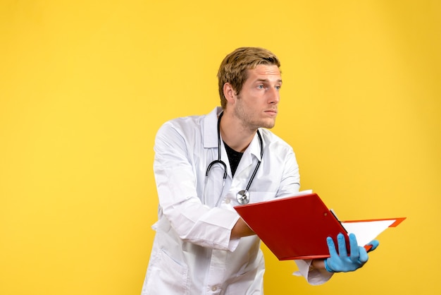 Vue de face de l'homme médecin tenant le fichier avec des notes sur le virus humain médical fond jaune