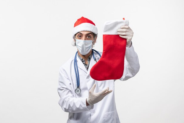 Vue de face de l'homme médecin tenant grosse chaussette de vacances sur mur blanc vacances virus covid