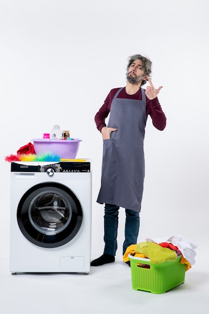 Vue de face homme de ménage confiant mettant la main dans la poche debout près d'une machine à laver blanche sur fond blanc