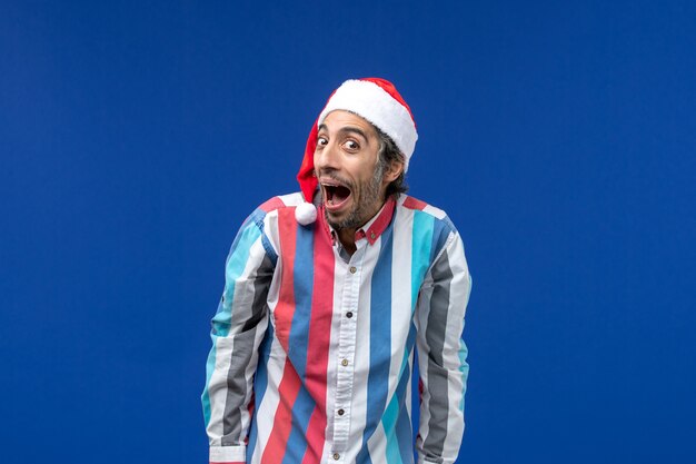 Vue de face homme ordinaire avec une expression excitée sur le bureau bleu des vacances de noël du père Noël