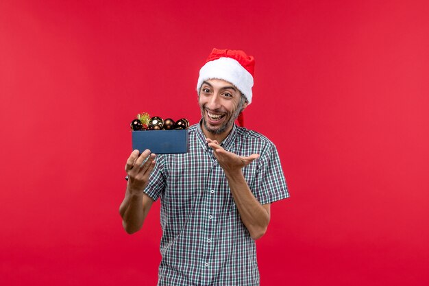 Vue de face d'un homme ordinaire avec des jouets d'arbre de Noël sur le rouge